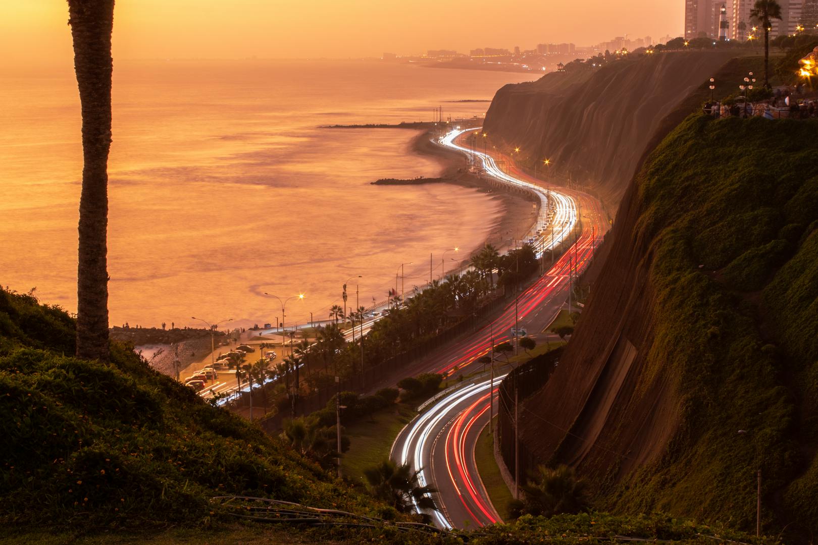 Atardecer sobre la costa de Lima con luces de tráfico bordeando el Pacífico, frente a Barranco, distrito bohemio de lujo.